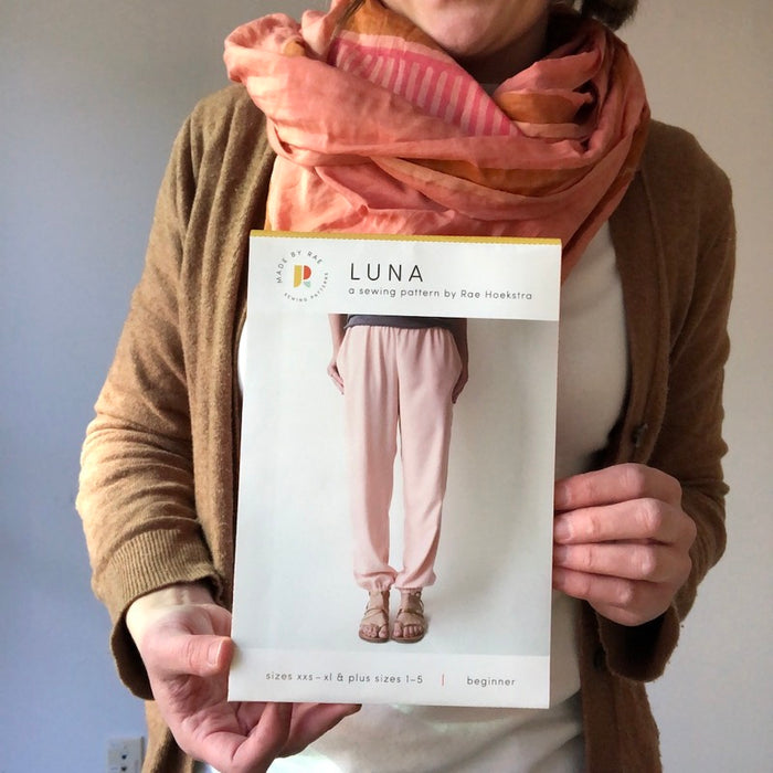 A person holds a printed Luna Pattern. They are wearing a pink scarf and brown sweater.